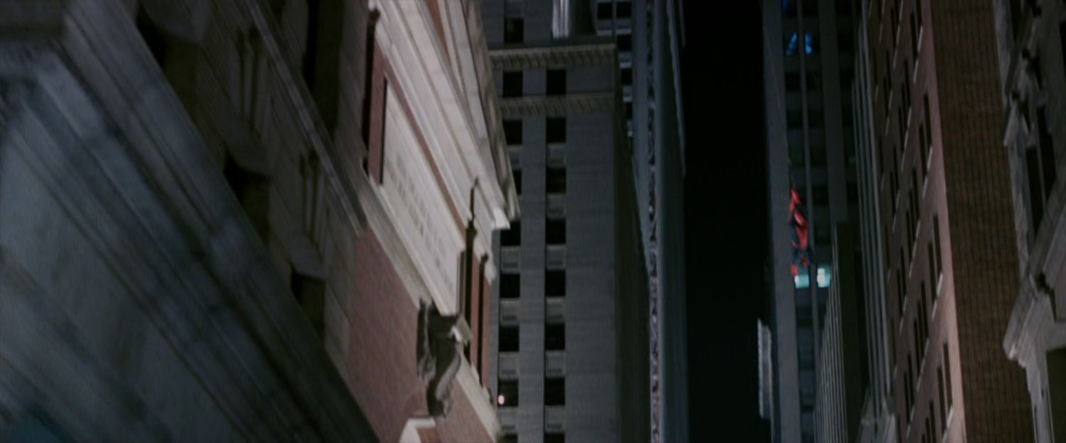 Spider-Man swings through a street at night.