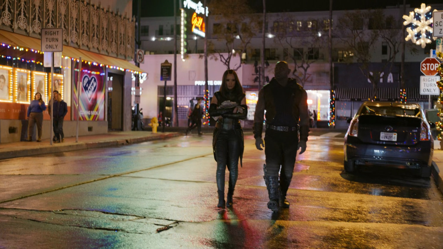 Mantis and Drax walk across a street at night.