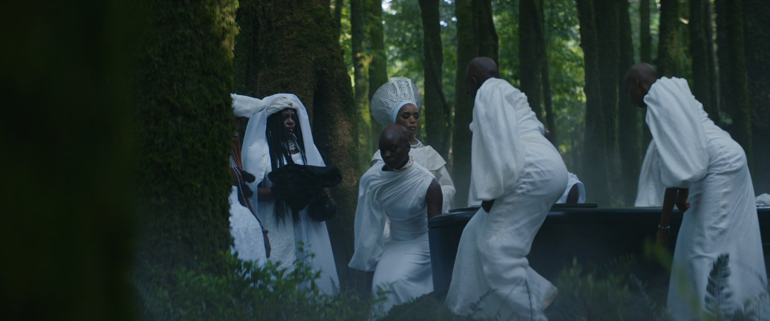Wakandans wearing white carry a coffin though the woods.