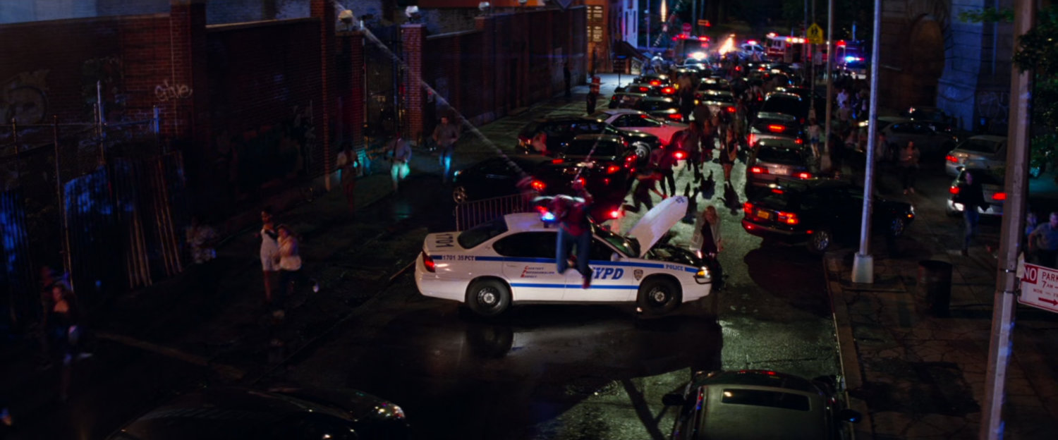 Spider-Man swings past a disabled police car.