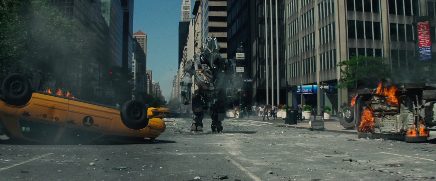 The Rhino stomps down a street with burning automobiles.