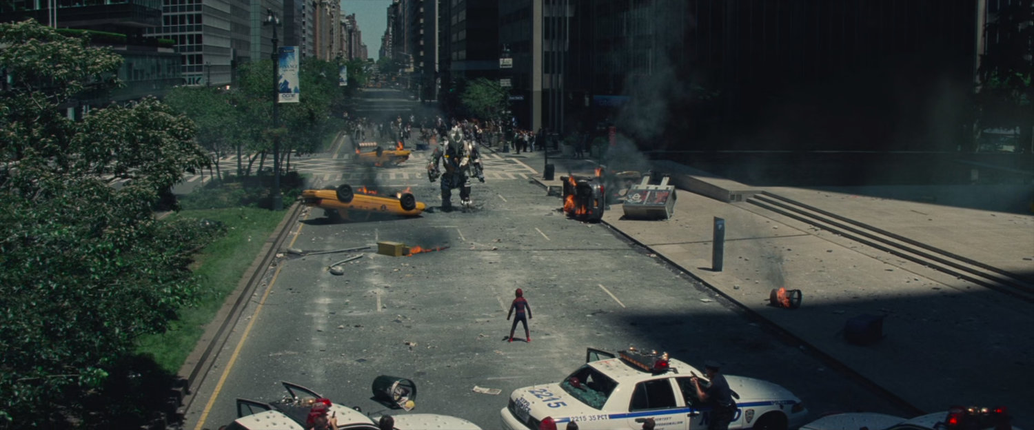 The Rhino stomps down a street with burning automobiles, confronted by Spider-Man.