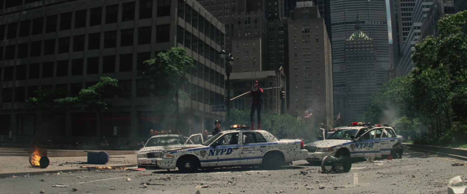 Spider-Man stands on a bullet-ridden police car with a megaphone.