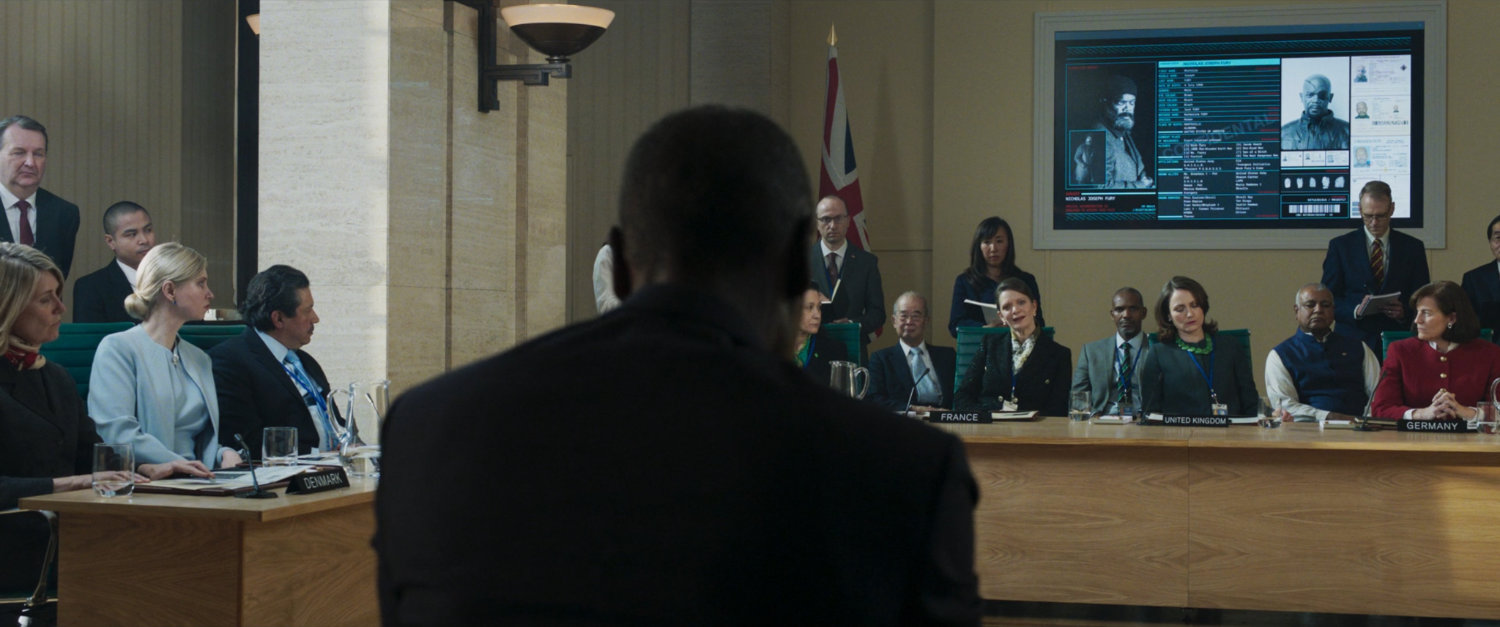 Colonel Rhodes facing a number of EU Leaders inside a small meeting chamber.