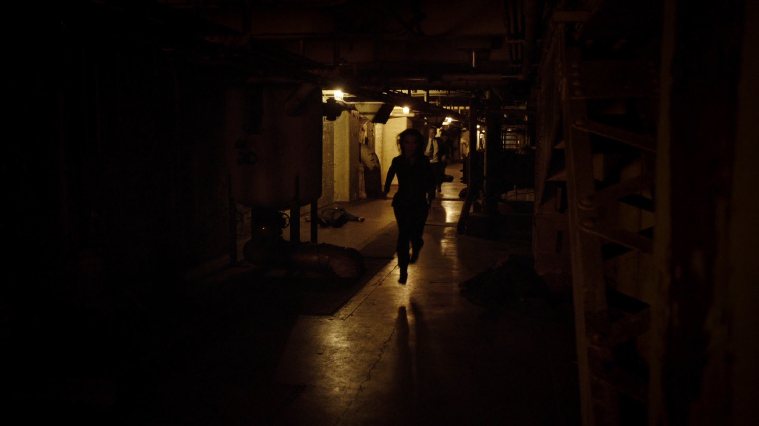 A silhouette runs through a dark underground tunnel.
