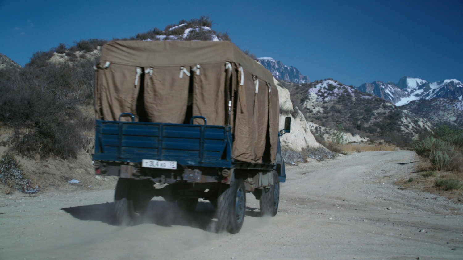 A covered truck driving on a dusty Caucasus Mountain road.