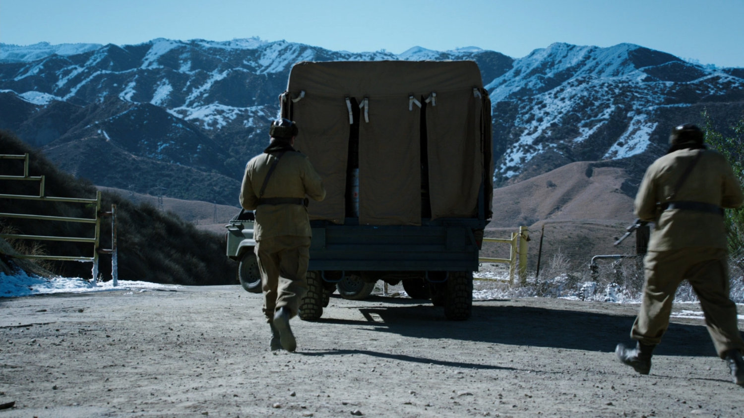 Two guards approach a covered truck at a Caucasus Mountain open area.