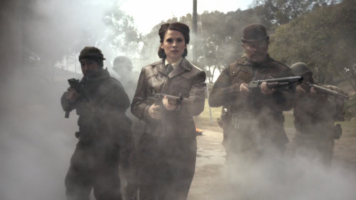 Peggy Carter and the Howling Commandos walking through smoke with guns drawn.
