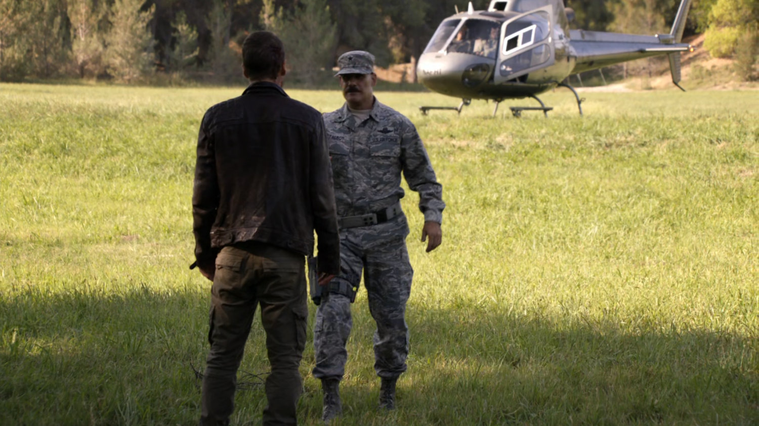 Hunter talking to Talbot in the middle of a field with Helicopter in background.