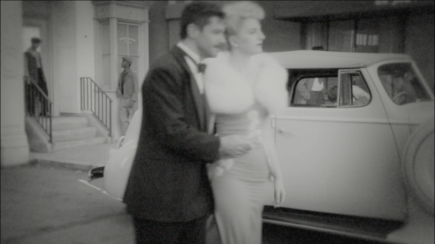 Howard Stark and woman walk past car.
