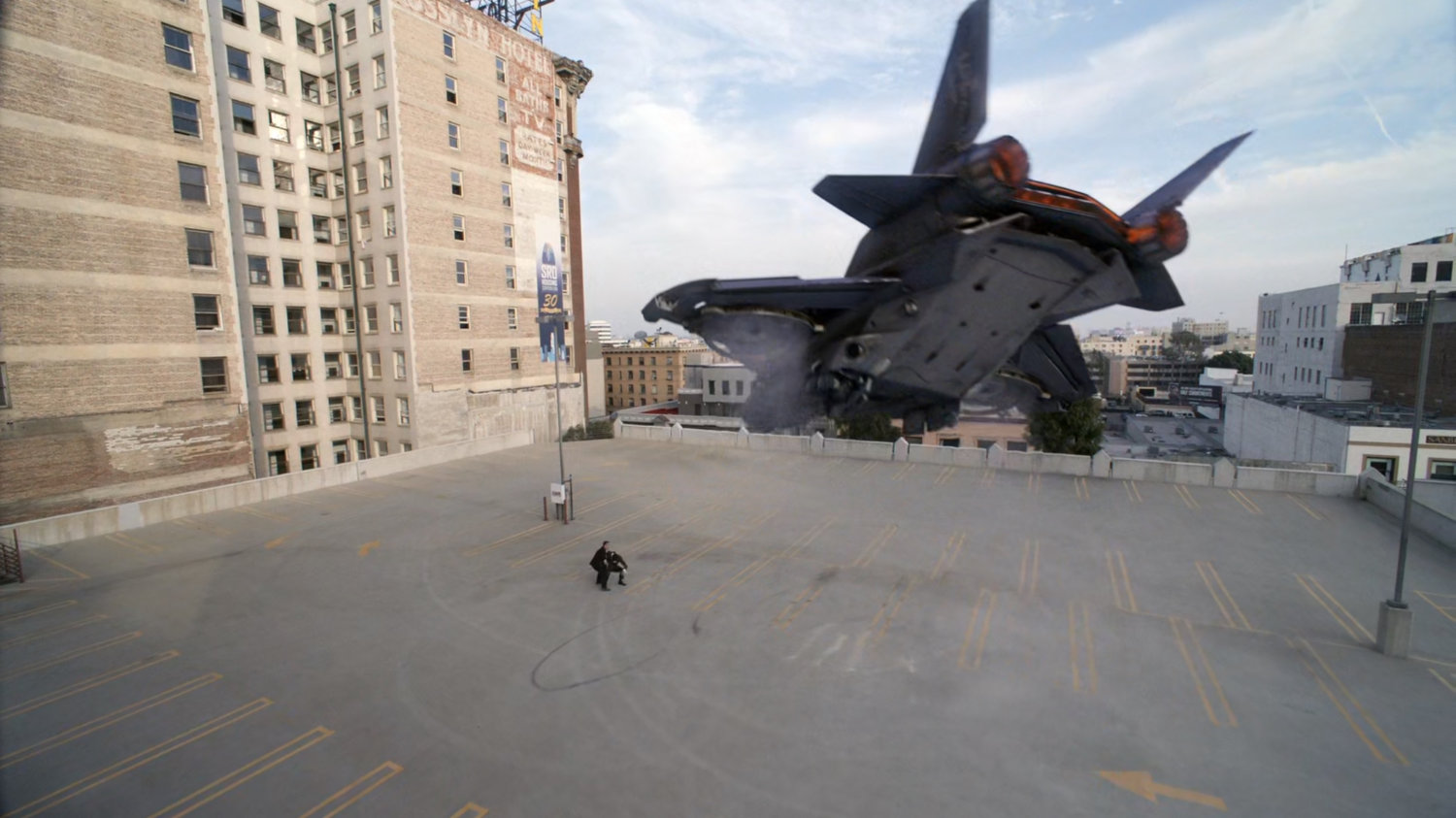 Man on parking garage roof deck watching quinjet take off.