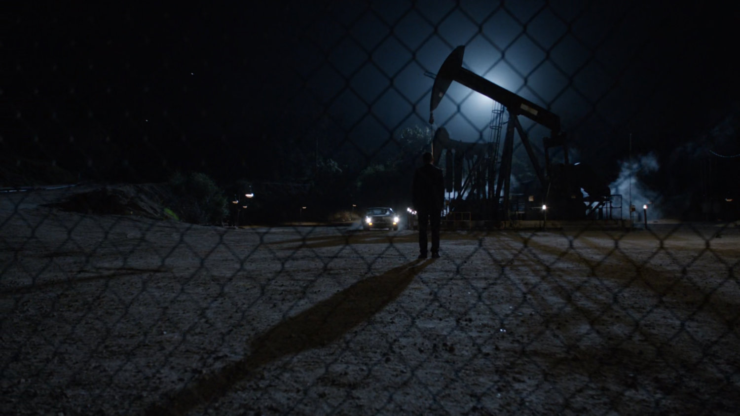Coulson in front of silhouetted oil derrick at night.
