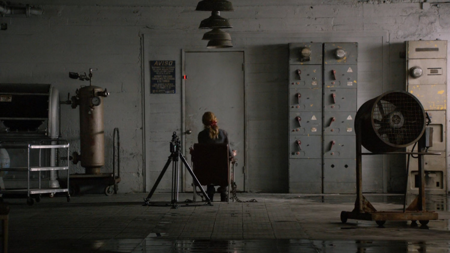 Bobbi bound and gagged in front of a door in an abandoned Spanish warehouse.