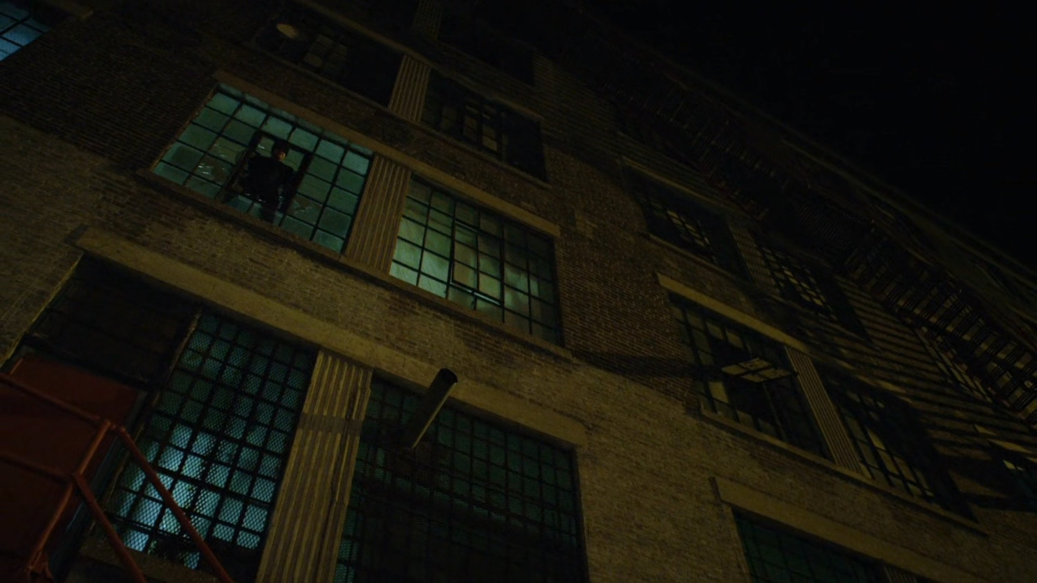 Daredevil looking into alley from broken window.