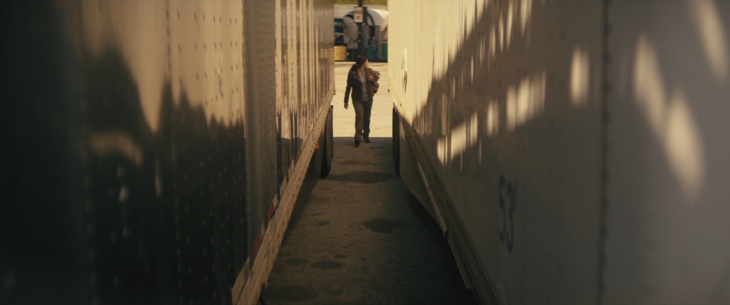 Maya walking between two semi trailers.