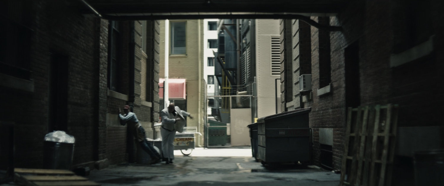 Kingpin throws ice cream vendor against an alley wall outside a private school.