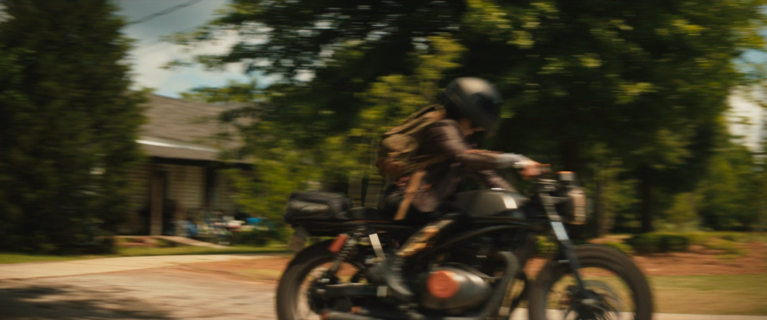 Maya pulling out of a driveway on her motorcycle.