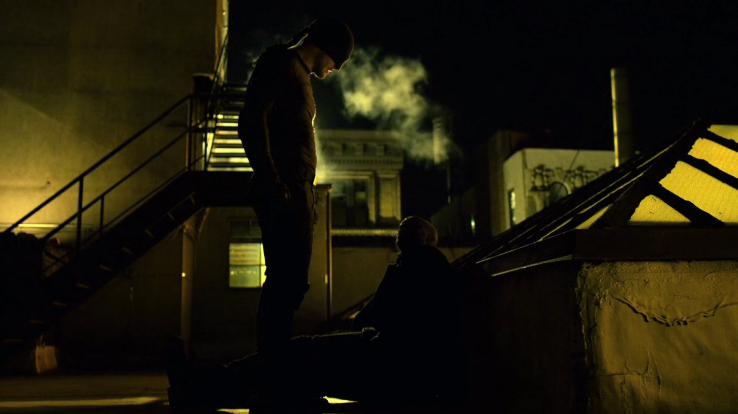 The Man in Black standing over Turk on a rooftop.