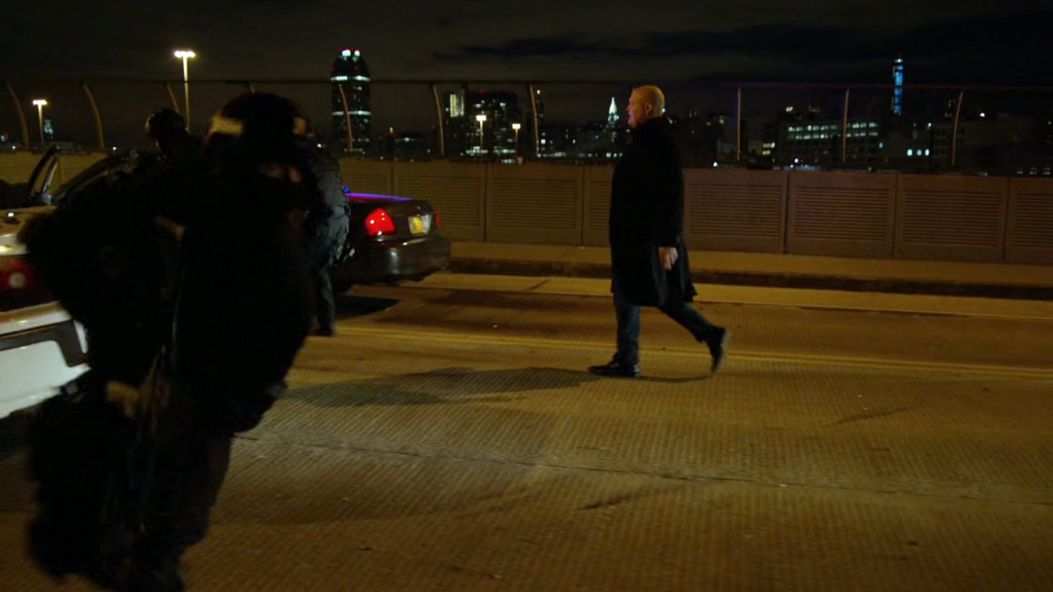Wilson Fisk walks down the center of a street on a bridge.