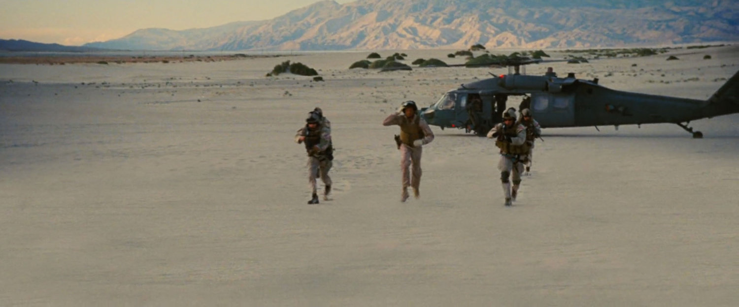 A helicopter and troops on a sand dune.