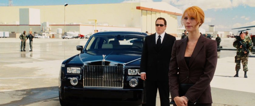 Pepper Potts and Happy Hogan wait by a limo on an airfield.