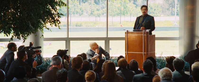 Tony Stark at a podium speaking to a crowd of reporters.