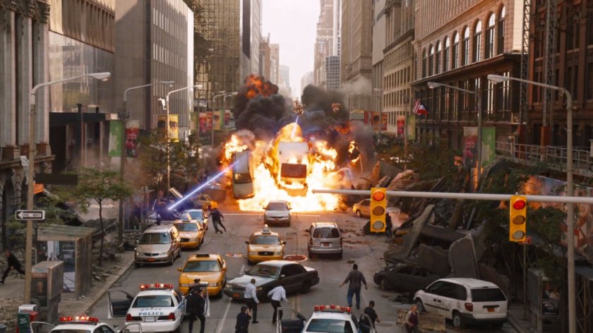 Vehicles explode in a city street while civilians look on.