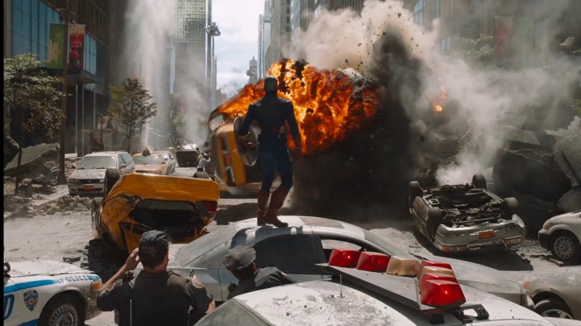 Captain America stands on a wrecked car surveying the explosions and damage.