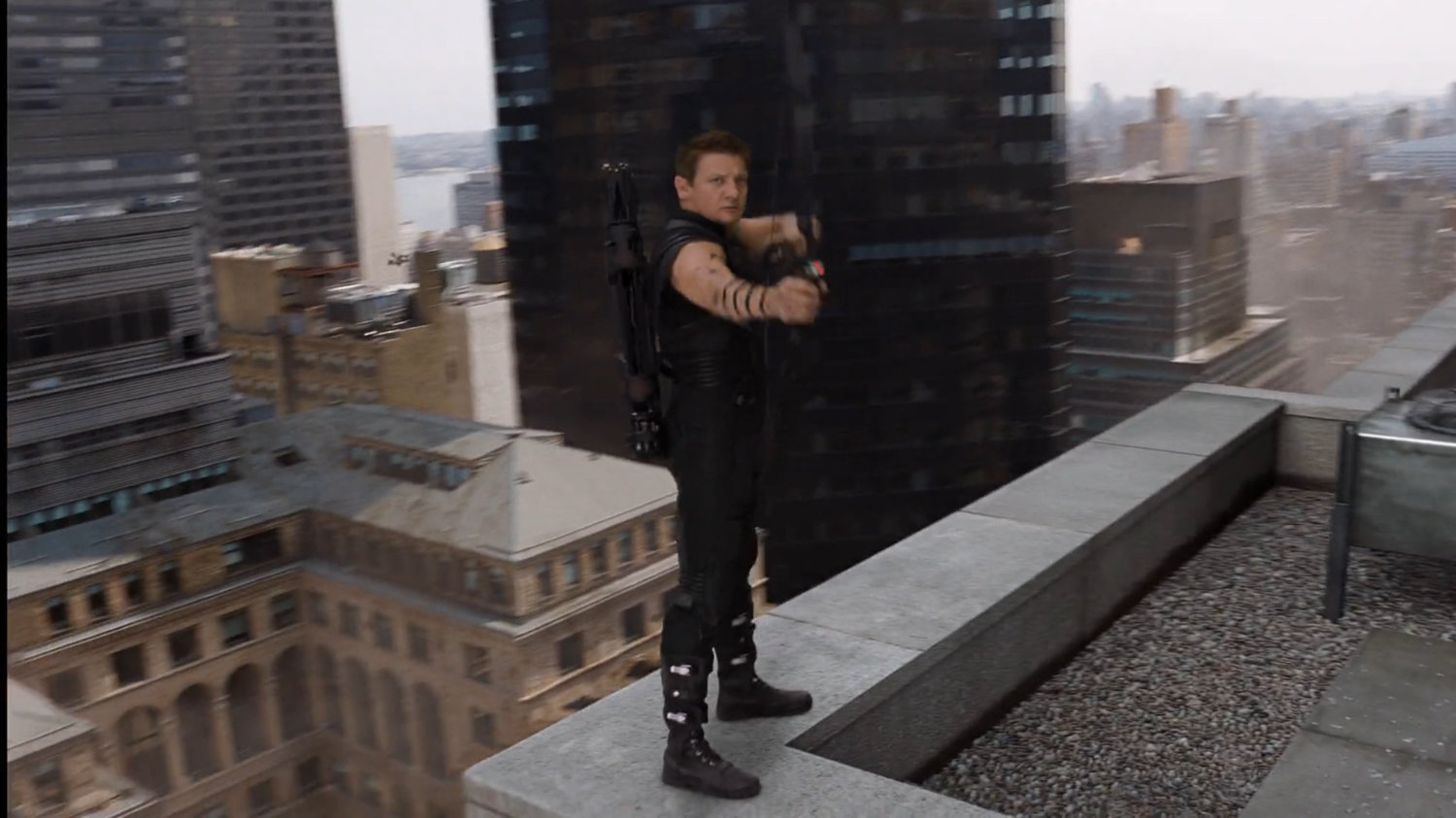 Hawkeye stands on the ledge of a rooftop, with his bow and arrow.