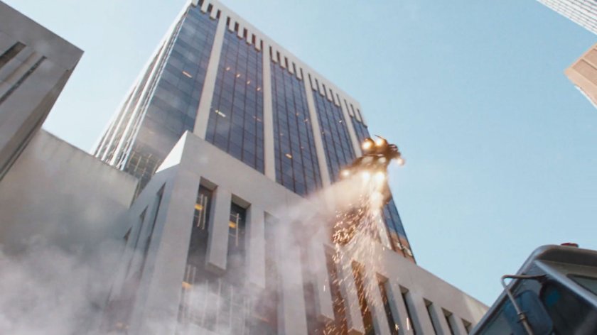 Iron Man blasts into the sky by a tall white building.