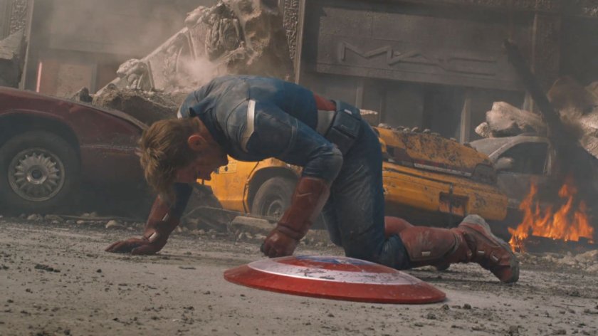 Captain America on his hands and knees on a debris filled street.