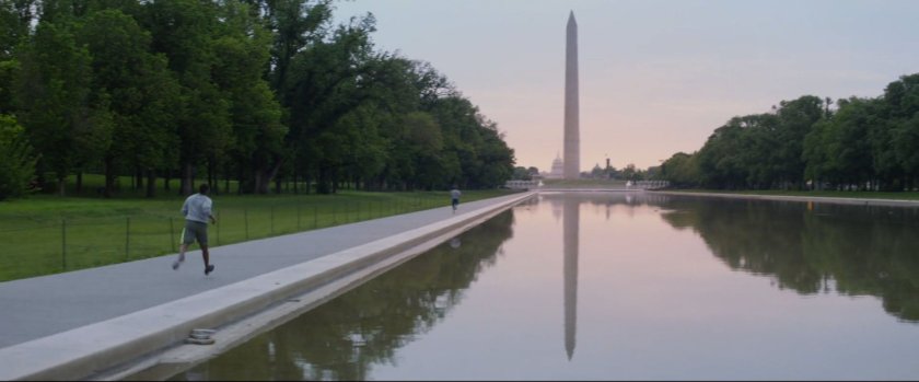 A man jogging along the reflecting pool with the Washington Monument in the distance.