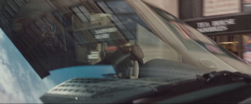 Nick Fury behind the wheel of SUV, driving on street.