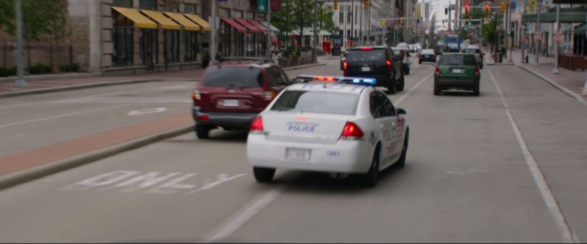Police car chasing black SUV on crowded city street.