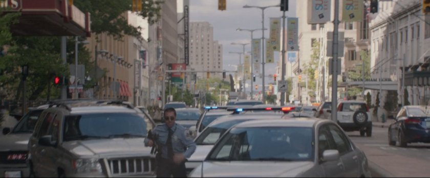 Police officer runs through parked cars on city street.