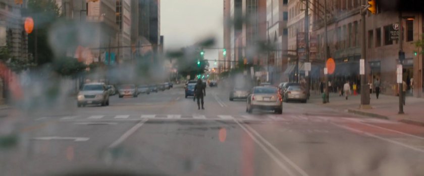 Man in middle of street as seen through cracked windshield.