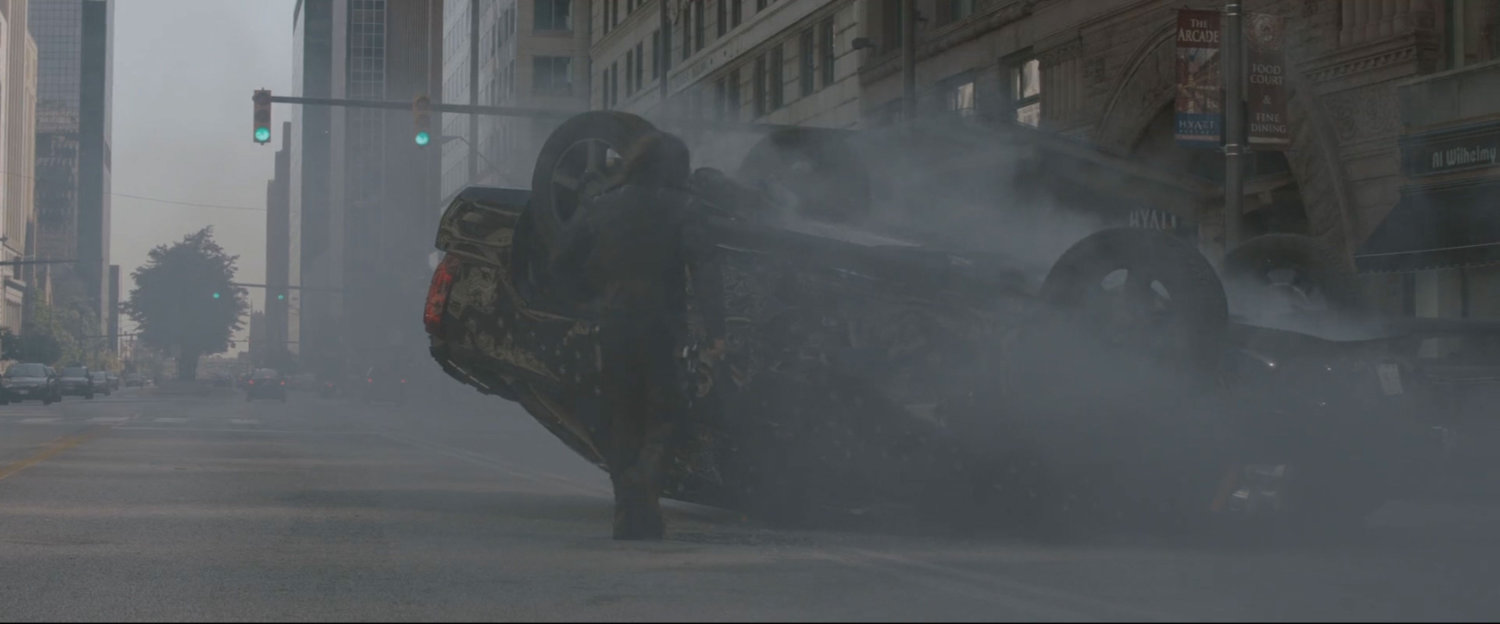 Man standing by inverted black SUV with smoke in the air.