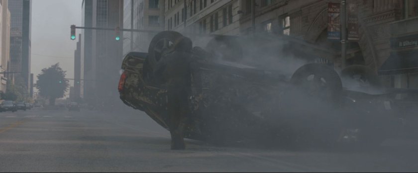 Man standing by inverted black SUV with smoke in the air.