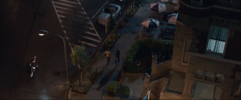 High angle of people walking on sidewalk and Steve Rogers pulling up on a motorcycle.