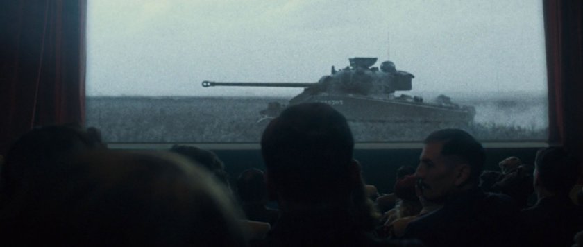 Audience in movie theater watching newsreel footage of tank.