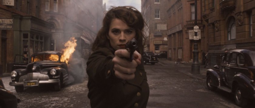 Peggy Carter stands with a pistol in the middle of a 1942 New York street.