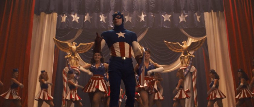 Captain America onstage with dancers inside a theater.