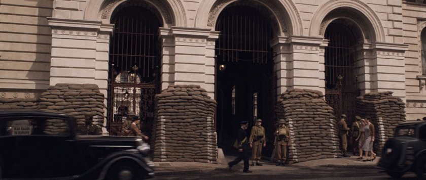 A building with three archways with sandbags set up in front of it.