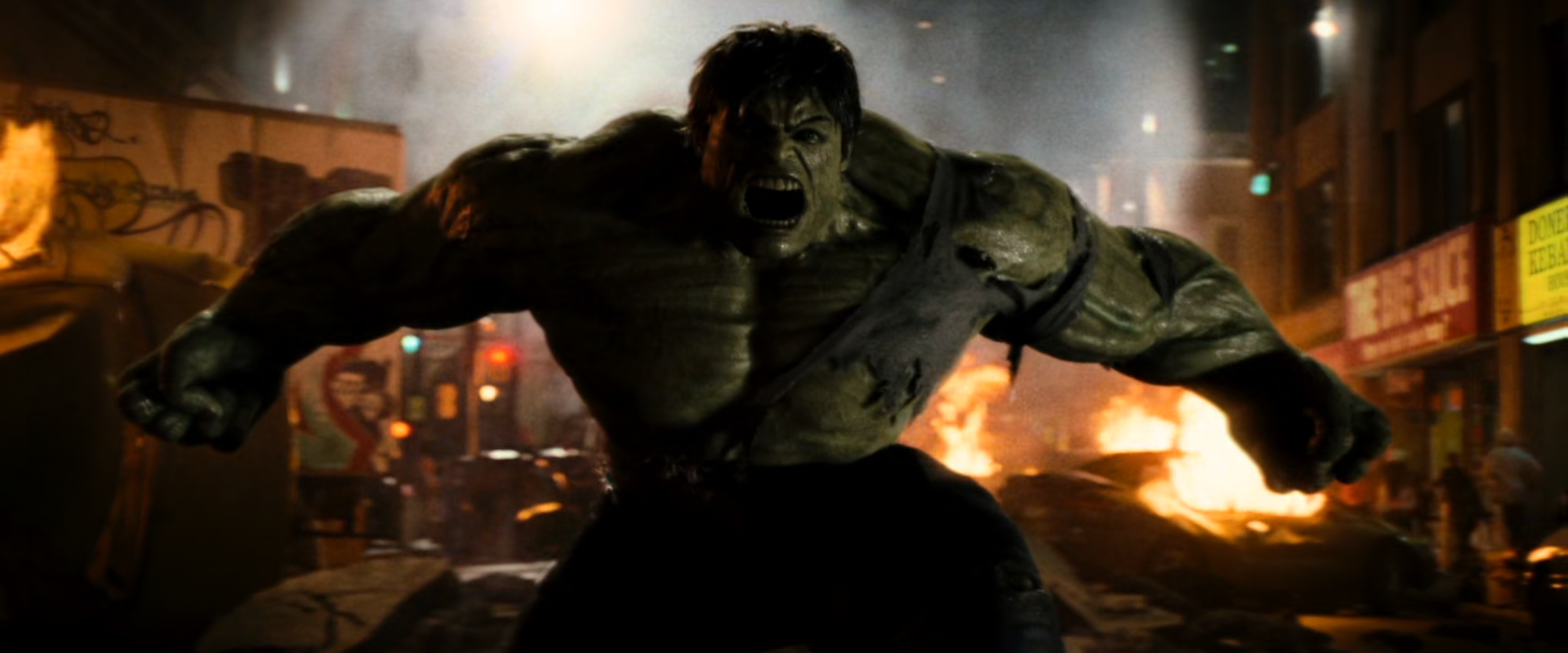 The Hulk roars in anger in front of flaming wreckage.