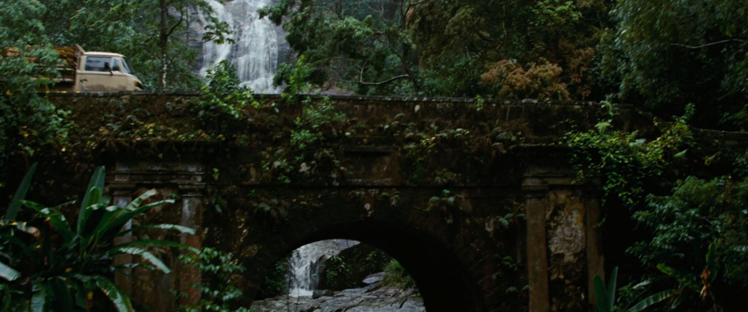 A bridge in front of a jungle waterfall.
