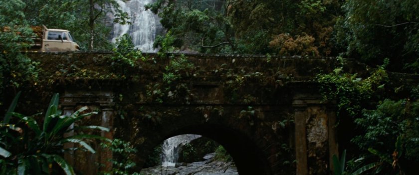 A bridge in front of a  jungle waterfall.