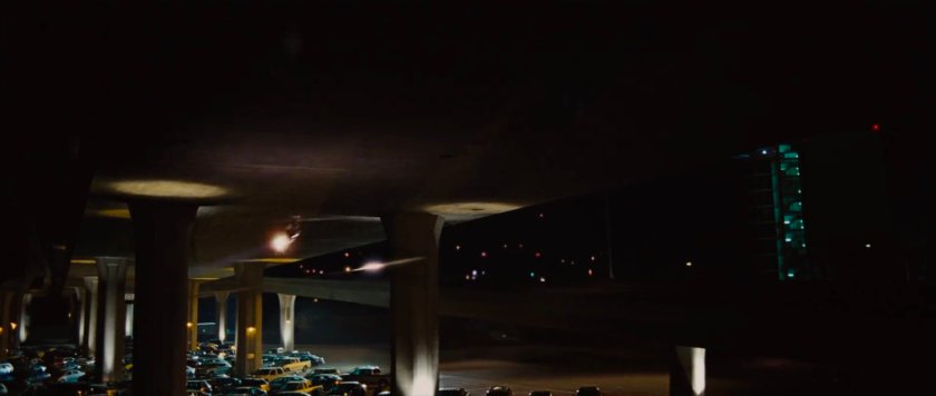 Nighttime under a freeway overpass with parked cars.