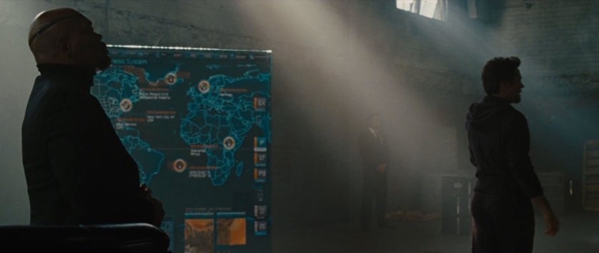 Nick Fury and Tony Stark in a smokey warehouse with a map of the world on a board behind them.