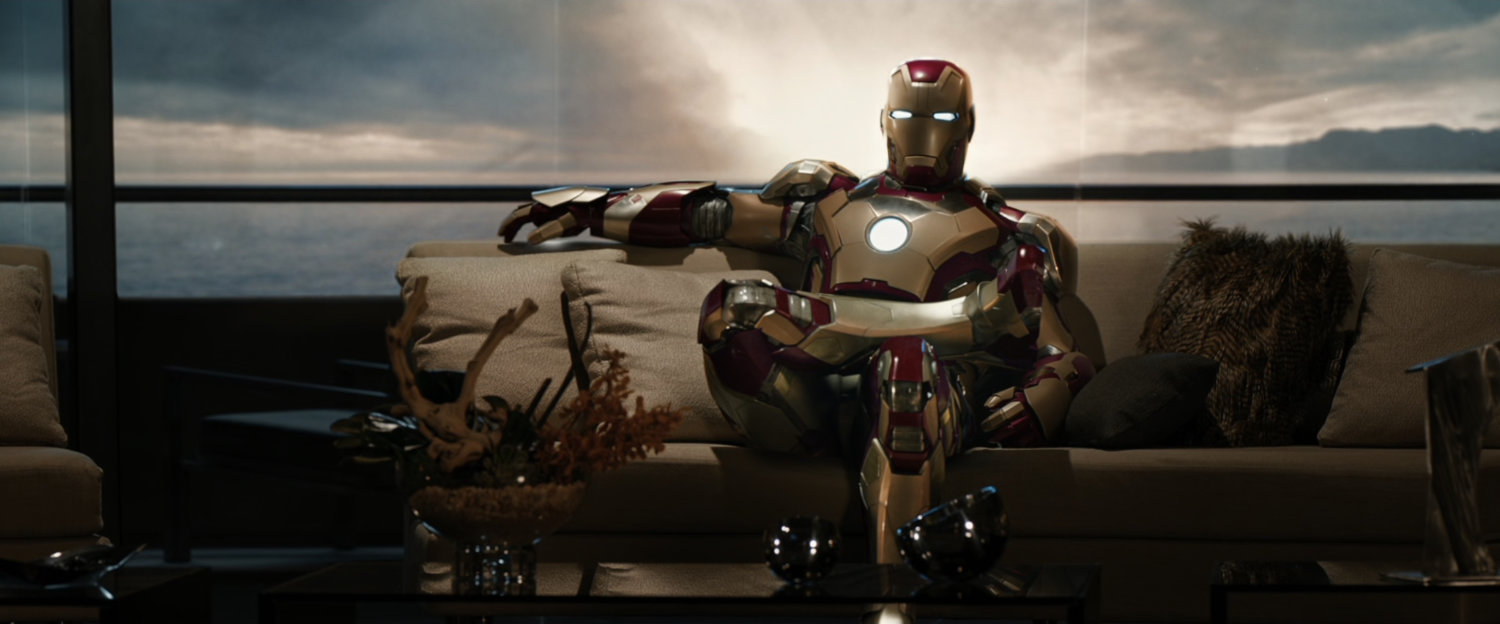 Iron Man sits cross legged on a couch.