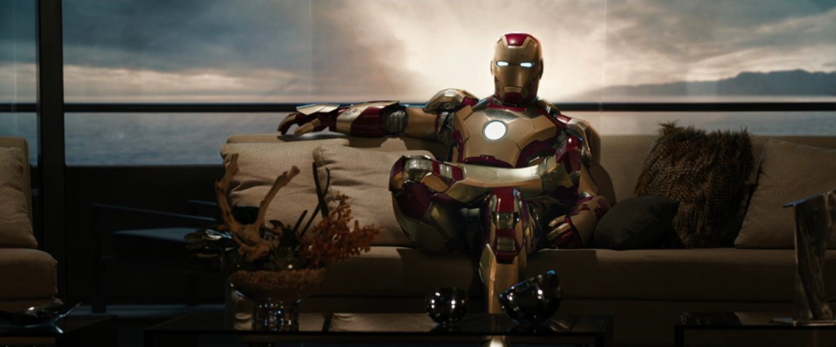 Iron Man sits cross legged on a couch.